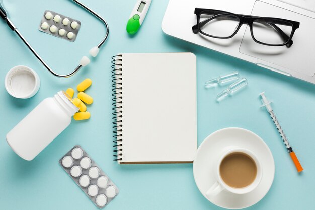 Healthcare supplies with notepad; cup of coffee and spectacles on laptop over table