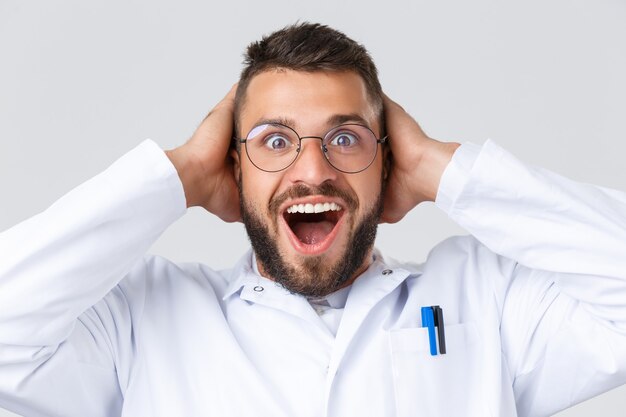 Healthcare workers, coronavirus, covid-19 pandemic and insurance concept. Close-up of excited happy doctor in white coat, glasses, cant believe own eyes, hold hands on head astonished