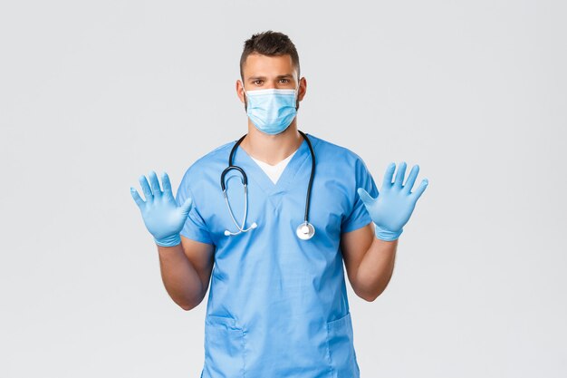 Healthcare workers, covid-19, coronavirus and preventing virus concept. Serious-looking hispanic doctor, male nurse in scrubs, medical mask, showing gloves on hands, ask wear protective equipment