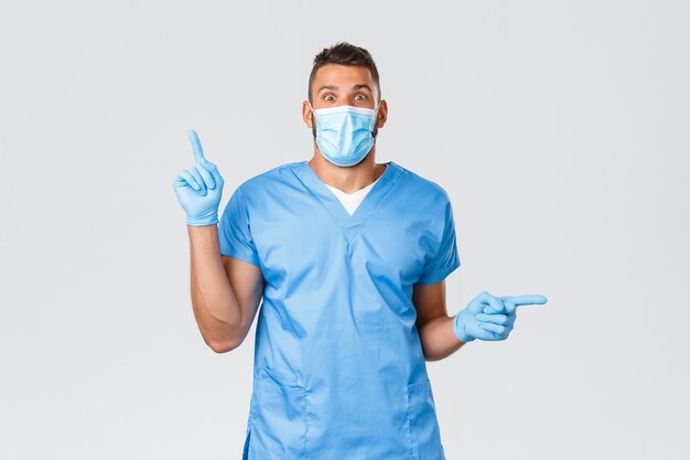 의료 종사자, covid-19, 코로나바이러스 및 바이러스 개념. 흥분한 남자 의사, 파란색 수술용 마스크와 의료 마스크를 쓴 간호사, 개인 보호 장비, 손가락을 옆으로 가리키는 두 가지 멋진 소식.
