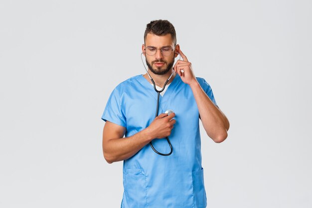 의료 종사자, 의학, covid-19 및 전염병 자가 격리 개념. 파란색 수술복을 입은 진지한 의사, 매일 환자를 검진하는 의사, 청진기를 사용하는 의사