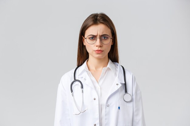 Healthcare workers, medicine, insurance and covid-19 pandemic concept. Skeptical and displeased, frustrated doctor in white scrubs with stethoscope, frowning and squinting at camera suspicious