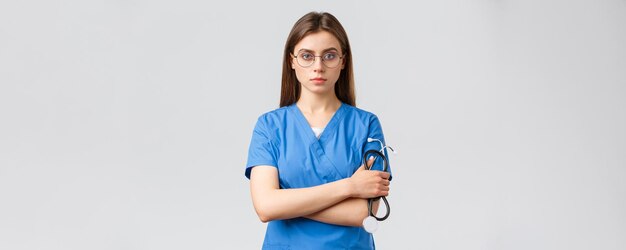 医療従事者の医療保険とcovid19パンデミックの概念聴診器を保持している青いスクラブの真面目で断固としたプロの女性看護師医師は自信を持って見えます