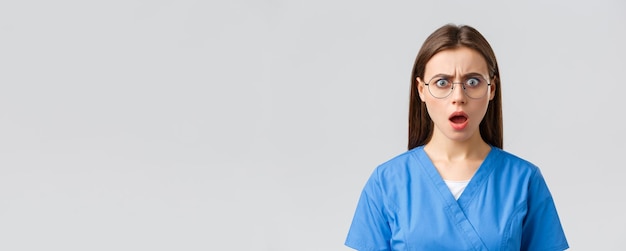 Healthcare workers medicine insurance and covid19 pandemic concept Shocked concerned female nurse doctor in blue scrubs and glasses say oh my gosh frustrated open mouth and frowning