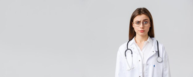 Healthcare workers medicine insurance and covid19 pandemic concept Skeptical and confused female doctor in white scrubs medical suit and glasses raise eyebrow judgemental smirk displeased