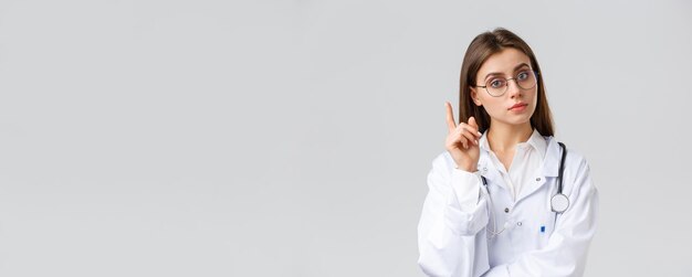 Healthcare workers medicine insurance and covid19 pandemic concept Smart professional female doctor in white scrubs and glasses have idea suggestion raise index finger eureka sign