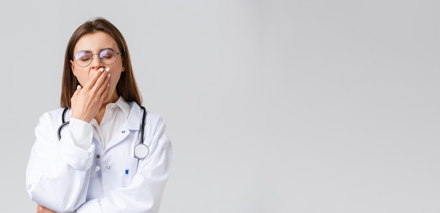 의료 종사자 의료 보험 및 covid19 전염병 개념 코로나바이러스 하품 및 입을 가리는 동안 열심히 야간 근무를 하는 흰색 수술 여성 의사의 젊은 의사