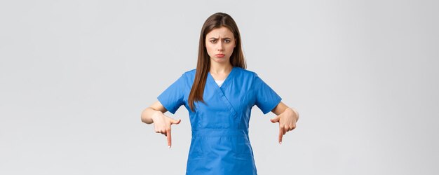 Healthcare workers prevent virus covid19 test screening medicine concept Disappointed and uneasy cute nurse or doctor in blue scrubs pointing fingers down showing bad unpleasant news