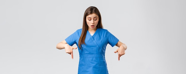 Healthcare workers prevent virus covid19 test screening medicine concept Impressed curious female nurse or doctor in blue scrubs pointing fingers down and looking at banner wondered