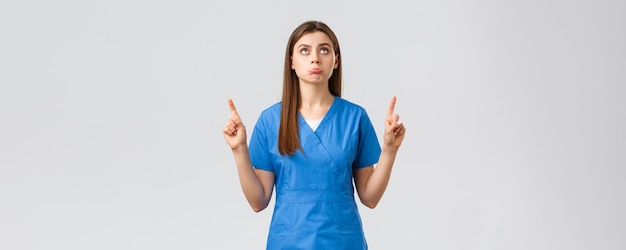 의료 종사자들은 바이러스 covid19 테스트 선별 의학 개념을 예방합니다. 어리석은 파란색 수술복을 입은 귀여운 의사 여성 간호사가 실망한 것을 가리키며 불쾌한 표정을 하고 있습니다.