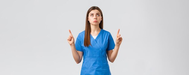 Healthcare workers prevent virus covid19 test screening medicine concept Silly upset cute doctor female nurse in blue scrubs pouting disappointed pointing and looking up displeased
