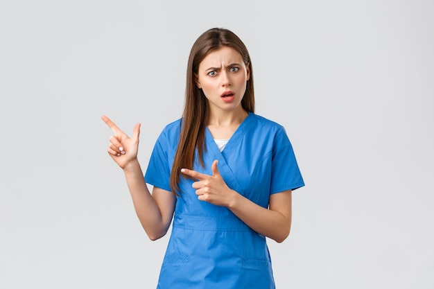 Healthcare workers, prevent virus, insurance and medicine concept. Concerned and puzzled nurse or doctor look confused, pointing fingers left, need answer, asking question, grey background