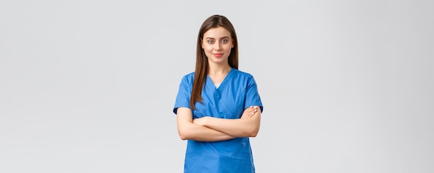 Healthcare workers prevent virus insurance and medicine concept Confident smiling female nurse doctor in blue scrubs cross arms chest and look determined Fighting covid19 outbreak stay home