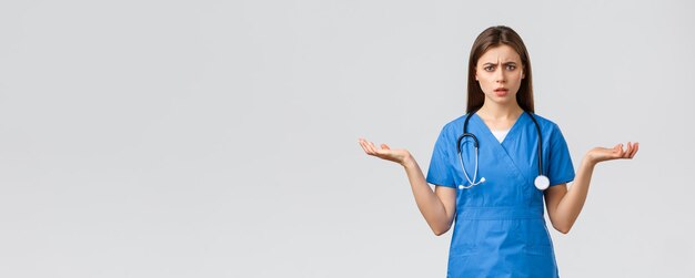 Healthcare workers prevent virus insurance and medicine concept Confused and puzzled female nurse doctor in blue scrubs spread hands sideways and shrugging cant understand