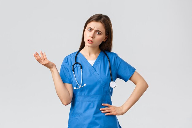 Healthcare workers, prevent virus, insurance and medicine concept. Confused and puzzled female nurse, doctor in scrubs with stethoscope, shrugging and lift hand, stare indecisive, cant understand