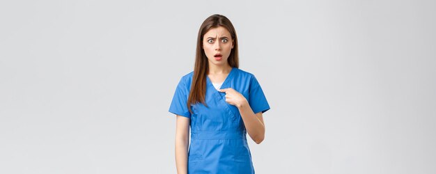 Healthcare workers prevent virus insurance and medicine concept Confused and shocked female nurse in scrubs pointing at herself gasping surprised cant believe being chosen or accused