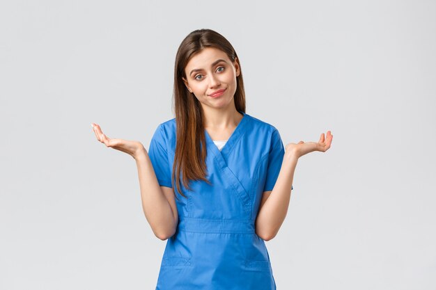 의료 종사자들은 바이러스, 보험, 의학 개념을 예방합니다. 의사가 말할 수 없다는 듯 어깨를 으쓱하고, 잘 모르겠습니다. 죄송합니다. 파란색 수술복을 입은 여성 간호사가 손을 옆으로 벌립니다.