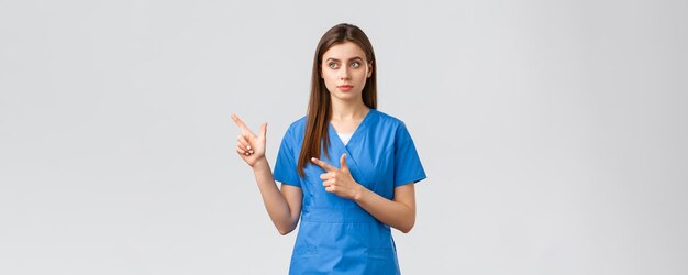 Healthcare workers prevent virus insurance and medicine concept Dreamy cute nurse or doctor in blue scrubs looking and pointing upper left corner reading banner info grey background