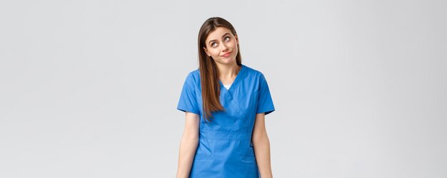 Healthcare workers prevent virus insurance and medicine concept Indecisive and unsure cute doctor female nurse in blue scrubs cant tell have no idea shrugging and look away uncertain