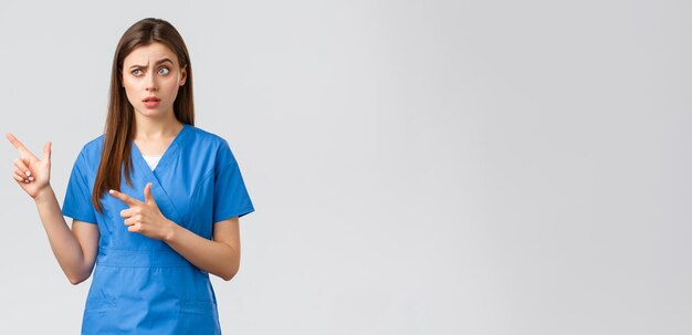 Healthcare workers prevent virus insurance and medicine concept Skeptical and unsure nurse or doctor in blue scrubs raise eyebrow suspicious pointing fingers left at banner