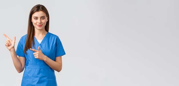 Медицинские работники предотвращают страхование от вирусов и концепцию медицины Улыбающаяся привлекательная женщина-врач или медсестра в синих халатах показывает пальцами влево, чтобы показать пациентам рекламу важную информацию
