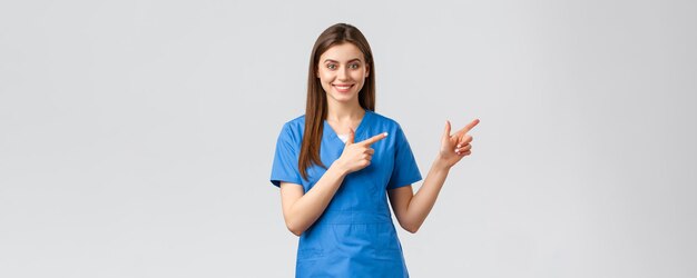 Healthcare workers prevent virus insurance and medicine concept Smiling nurse or female doctor in blue scrubs pointing fingers down inform about coronavirus news show information