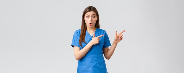 医療従事者はウイルス保険と薬の概念を防ぎます青いスクラブで驚いた看護師または医者はカメラにショックを受けた右あえぎ指を指している興味深いニュースを聞きます
