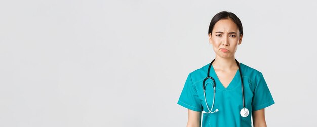 Healthcare workers, preventing virus, quarantine campaign concept. Close-up of skeptical and reluctant female asian physician, medical worker in scrubs looking displeased, white background