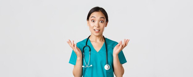 Healthcare workers, preventing virus, quarantine campaign concept. Close-up of surprised and amused, happy asian female nurse, physician hear great news, raise hands amazed and look camera