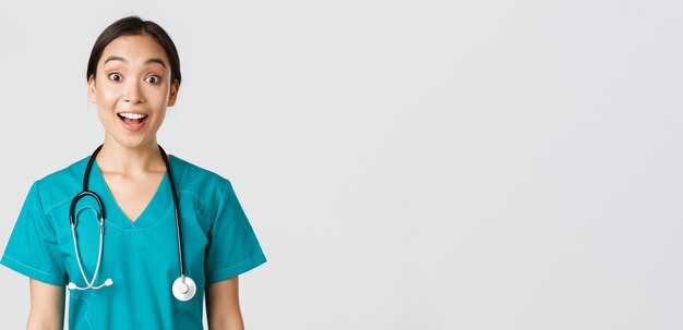 Healthcare workers, preventing virus, quarantine campaign concept. Happy and excited asian female doctor, physician in scrubs look amazed, hear awesome news, white background