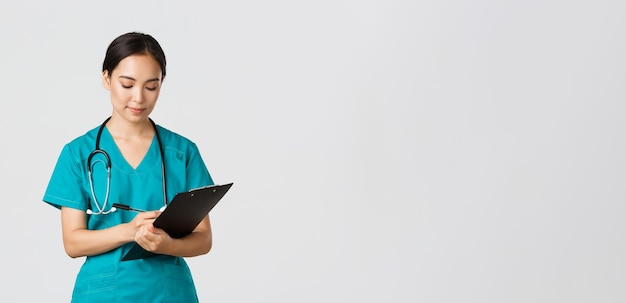 Free photo healthcare workers, preventing virus, quarantine campaign concept. serious-looking professional female doctor, nurse in scrubs writing down info on clipboard, examine patient, white background