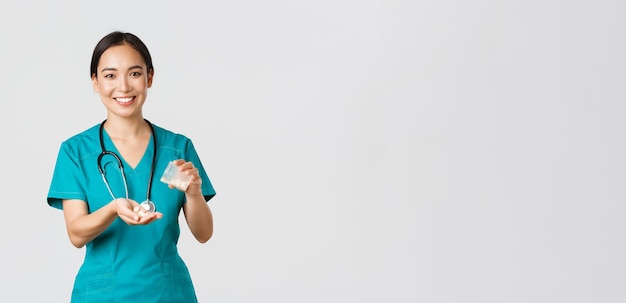 Free photo healthcare workers, preventing virus, quarantine campaign concept. smiling friendly asian female doctor, physician in scrubs, give patient medication from container, white background