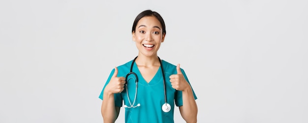 Free photo healthcare workers, preventing virus, quarantine campaign concept. young supportive asian nurse give thumbs-up. doctor cheer-up patient, encourage someone or compliment, white background