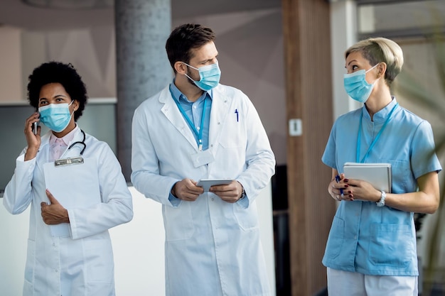 Healthcare workers with face masks talking while walking through a hallway at the hospital