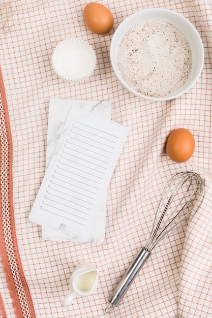 キッチンナプキンの上の空のチェックリストと健康的なベーキング成分