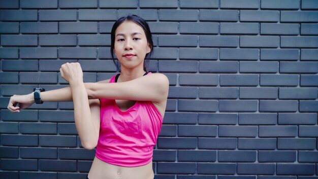 スポーツウェアの足の健康的な美しい若いアジアアスリート女性彼女の腕を温めとストレッチ