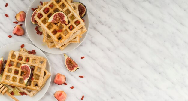 Healthy belgian waffles; fig; honey; and honey dipper served in plate against marble floor