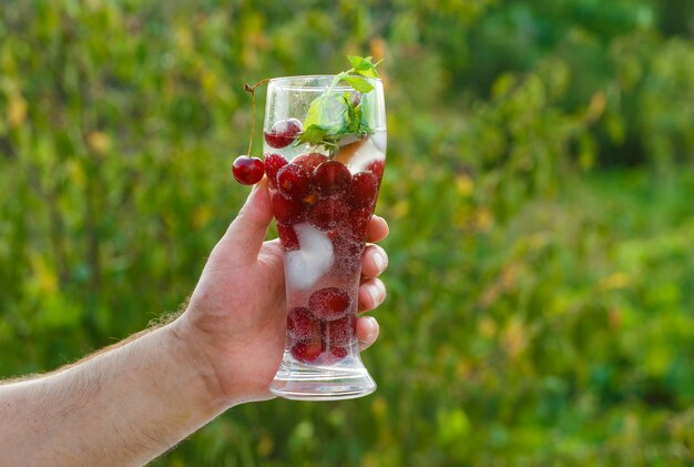 Healthy beverage concept on green background side view. hand holding glass of cocktail.