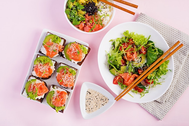 Healthy breakfast. Buddha bowl with rice, mango, avocado and salmon and fresh salad with tomatoes, avocado, arugula, seeds, salmon and salmon sandwich with avocado, creame cheese and microgreen. Healt