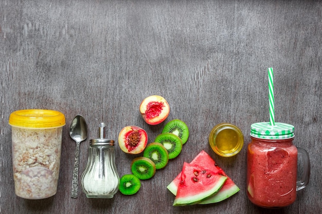 Healthy breakfast: fresh smoothie in glass jar with oatmeal granola, kiwi and watermelon on dark wooden background