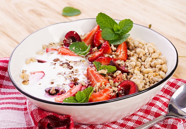 Healthy breakfast - granola, strawberries, cherry, nuts and yogurt in a bowl on a wooden table. Vegetarian concept food.