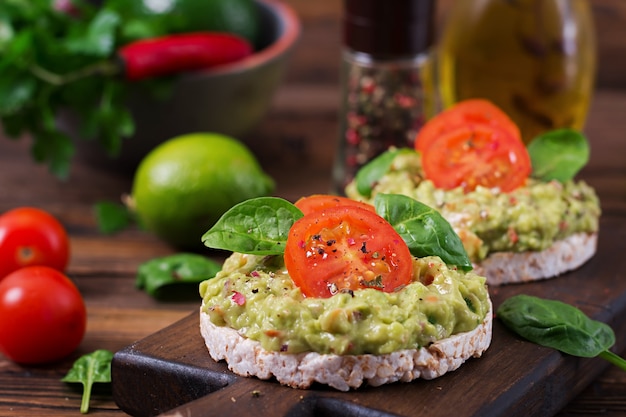 Healthy breakfast. Sandwich crisp bread with guacamole and tomatoes on a wooden table.