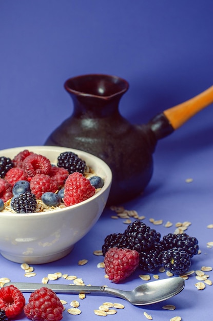 Здоровый завтрак. Белая тарелка с разбросанной овсянкой и разными ягодами на синем фоне.
