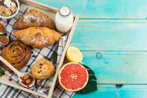Бесплатное фото Здоровый завтрак с круассаном; резервное печенье; молоко; мюсли; и цитрусовые на деревянном подносе