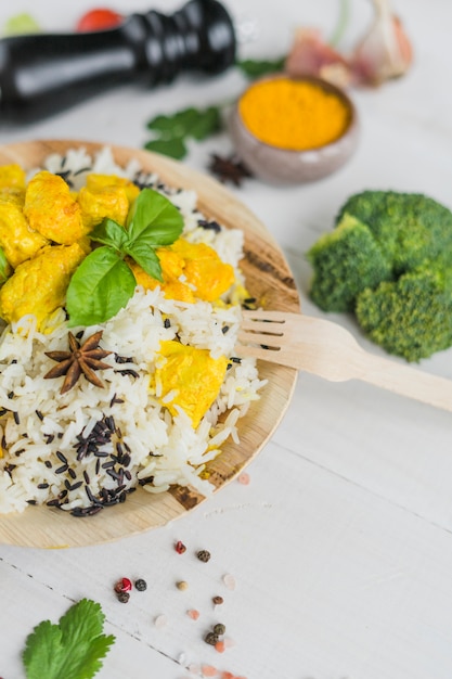 Healthy chicken fried rice; basil leaves in plate with wooden fork and vegetables