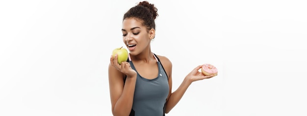 건강하고 다이어트 개념 아름다운 스포티한 아프리카계 미국인은 도넛과 녹색 사이에서 결정을 내립니다