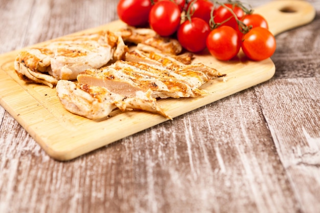 Healthy diet. Fresh grilled chicken breast on wooden board next to tomatoes. Healthy dinner and lifestyle