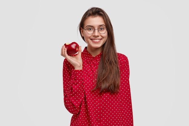 健康的な食事の概念。かなり若い女性は新鮮な赤いリンゴを食べ、健康的なライフスタイルを導き、生の菜食主義の有機食品を楽しんでいます