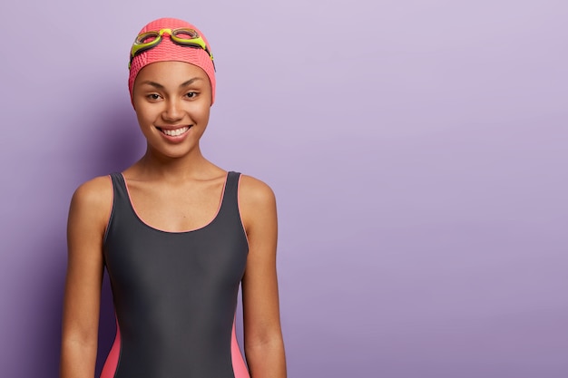 健康な女性のスイマーはピンクのキャップ、ゴーグル、水着を着て、プールでのトレーニングの準備をします