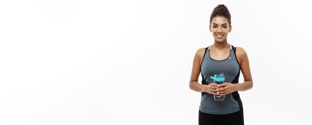 Healthy and Fitness concept beautiful African American girl in sport clothes holding water bottle after workout Isolated on white studio background